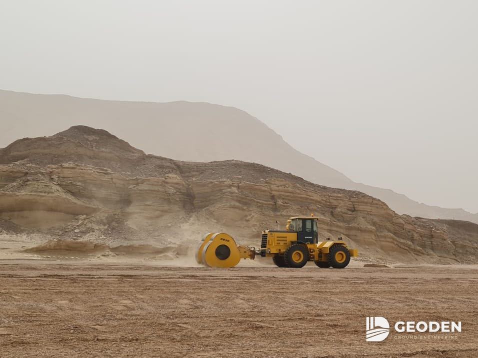 جرار يقطر أسطوانة صدم غير دائرية في موقع صحراوي عند سفح تلال صخرية